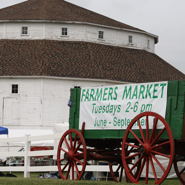 Historical White Round Barn with a Green Wagon with Red Wheels with a sign that says "Farmers Market"